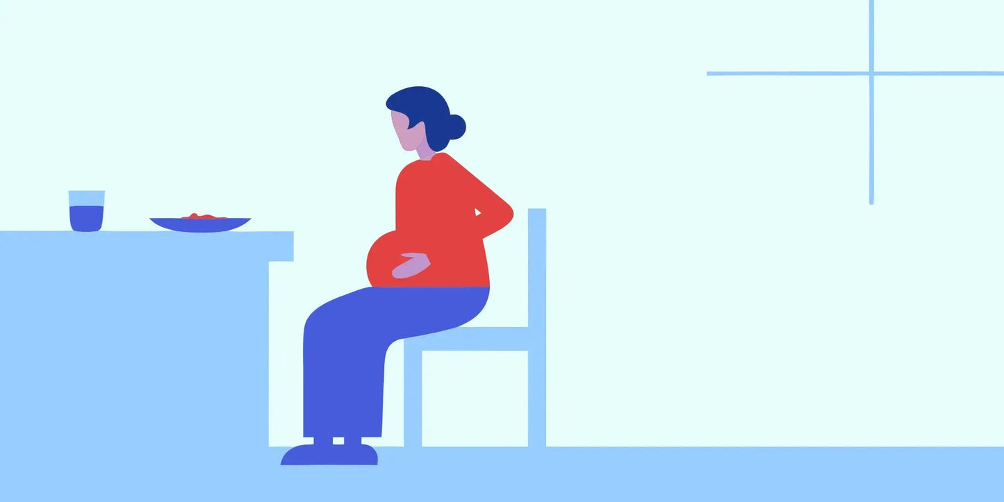 Senior woman sitting at kitchen table with hand on her abdomen after a meal, looking uncomfortable