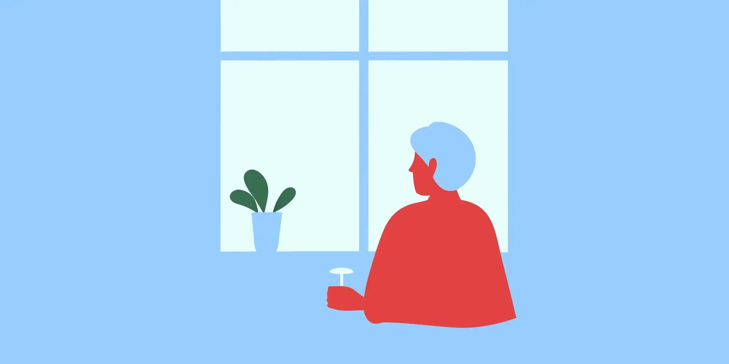 Senior woman sitting at a kitchen table holding a supplement bottle and glass of water in warm natural light